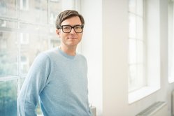 Portraitfoto eines Mannes, der an einer Fensterbank lehnt.